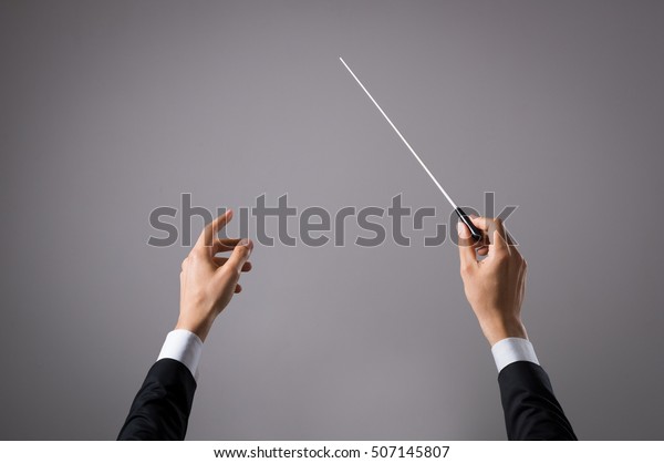 Concert conductor hand with baton isolated on grey\
background. Chorus composer holding baton during a opera. Musician\
directing concert. Close up hands of orchestra conductor with copy\
space.