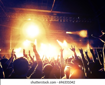Concert crowd attending a concert, people silhouettes are visible, backlit by stage lights. Raised hands and smart phones are visible here and there. - Shutterstock ID 696331042