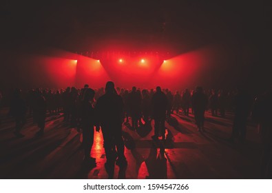 Concert crowd background.Group of young people on dance floor in music hall.Techno music party poster.Bright red stage lights in night club. Entertainment event in Ukrainian nightclub.