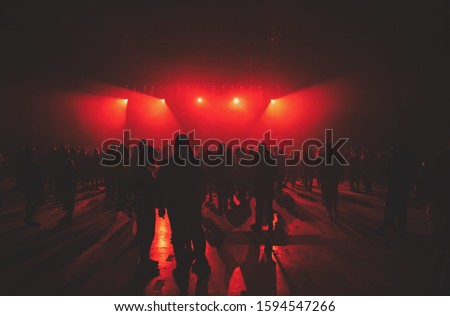 Concert crowd background.Group of young people on dance floor in music hall.Techno music party poster.Bright red stage lights in night club. Entertainment event in Ukrainian nightclub.