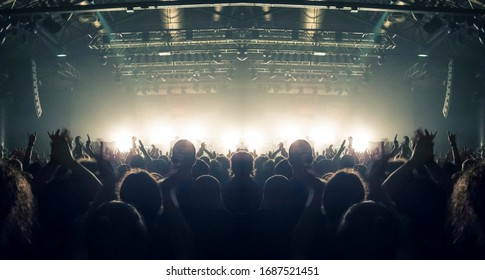 Concert Crowd Point Of View Inside A Large Concert Hall During A Music Festival, The Lit Stage Is Visible.