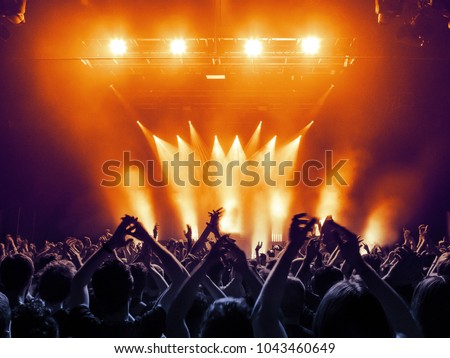 Concert hall with a lit stage and people silhouettes during a concert