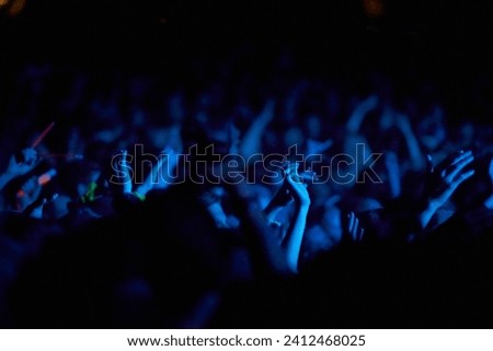 Concert, hands and audience for music with blue lights, neon and night festival, concert or psychedelic party. Crowd with arms raised with nightlife and rave or techno event for new year holiday