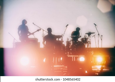 Concert of a musical rock band. Silhouettes of musicians on a set background. Blurred background.