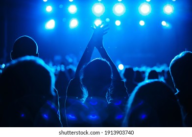 Concert silhouette of happy young woman partying on live event in crowded music hall.Curated shutterstock concert collection.Big group of young people partying on dance floor in night club.