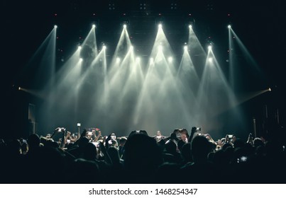 Concert stage lights  crowd on dance floor partying to the music.Group of young people with smartphones having fun on dancefloor in nigth club.Bright stage lights and silhouettes of fans with phones 