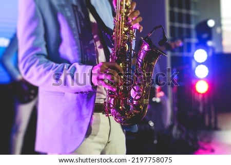 Concert view of saxophonist, a saxophone sax player with vocalist and musical band during jazz orchestra show performing music on stage in the scene lights
