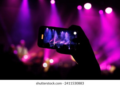 A concert-goer captures the live performance of a band on their phone. - Powered by Shutterstock