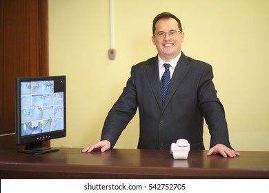 Concierge Behind The Counter At His Workplace Near The Telephone In A Luxury Apartment Building