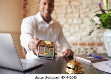 Concierge At Hotel Reception Holds Credit Card Reader To Camera