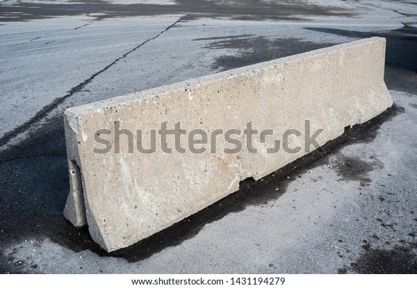 Concrete barrier on dirty\
empty asphalt.