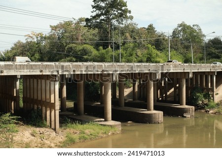 concrete Bridge Spanning Serene River in Nature Landscape with Sky, Road, and Trees