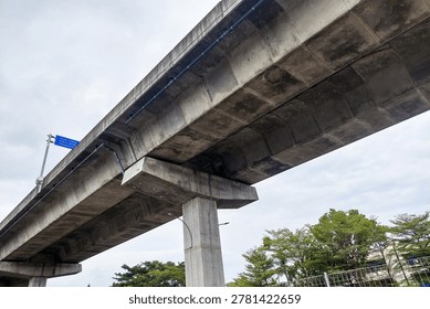 Concrete bridge spans skyward with solid pillars. Gray structure stands tall against soft clouds.