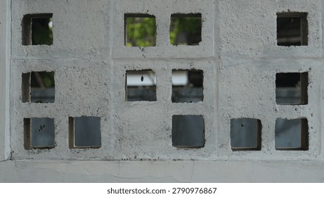 Concrete building facade featuring multiple square windows, some with visible greenery inside, showcasing urban architecture and design elements.