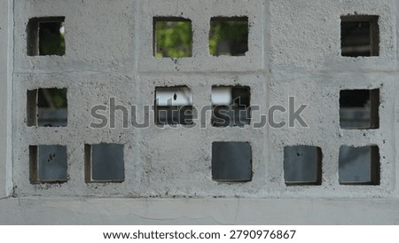 Concrete building facade featuring multiple square windows, some with visible greenery inside, showcasing urban architecture and design elements.