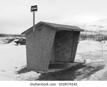 Concrete Bus Stop Shelter With Bus Sign On Pole. Winter Scene With Snow And Ice. Black And White Photo 