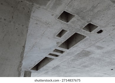 Concrete ceiling showing multiple rectangular cutouts and rough unfinished surface, construction site featuring exposed structural elements and geometric openings in raw material
