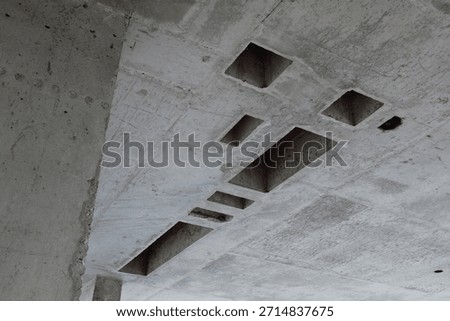 Concrete ceiling showing multiple rectangular cutouts and rough unfinished surface, construction site featuring exposed structural elements and geometric openings in raw material