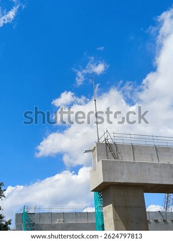 Concrete column structure of an elevated toll road under construction, with temporary scaffolding and weather monitoring equipment installed on top. Clear blue sky in the background.