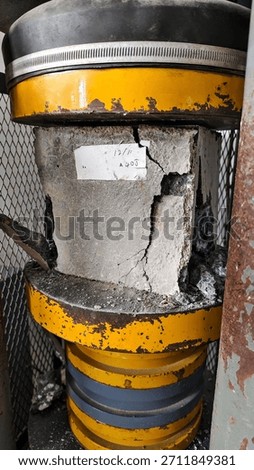 Concrete cube specimen undergoing compression strength test in laboratory. Visible crack formation indicates structural failure analysis for quality control in construction engineering.
