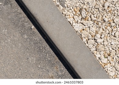 A concrete curb with a gravel border. The gravel is scattered around the curb and is not in a neat line