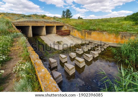 Concrete discharge sluice in earthen dam on small river in countryside. Hydraulic structure for preventing water reservoir from overflow. Stock fotó © 