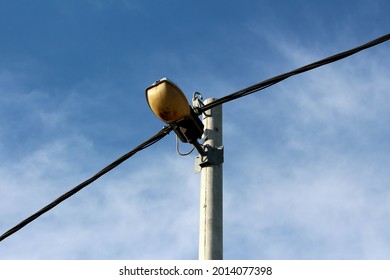 Concrete Electrical Utility Pole With Thick Black Electrical Wires And Old Antique Retro Vintage Street Lamp On Cloudy Blue Sky Background