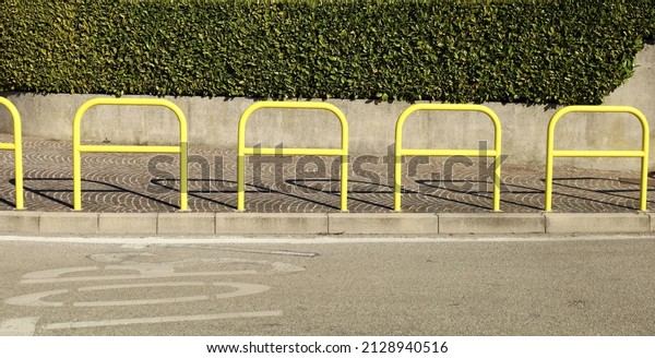 Concrete enclosure wall with green hedge above.\
Porphyry sidewalk, yellow pedestrian barrier and asphalt road in\
front. Background for copy\
space