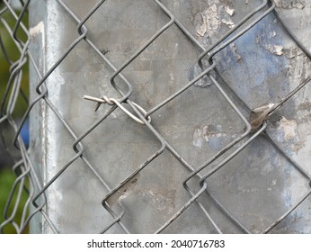 Concrete Faceted Rough Post Is Wrapped In Steel Mesh With Square Cells. Interlacing And Assembly Of Metal Wire. Abstract Image Background. Focus On Middle Plan With  Shallow DOF.
