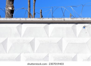 a concrete fence with barbed wire and a blue sky in the background with chopped trees. (you can draw your graffiti on the wall)