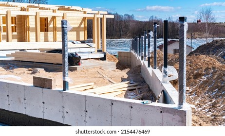 Concrete foundation with drainage holes of the fence for a modern wooden house made of glued laminated timber. Construction of a house on the shore of a forest lake in spring.