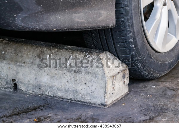 Concrete grey parking stoppers with auto tire in\
parking lot.