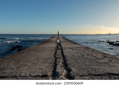 Concrete jetty with no people reaching away into the calm seas of the Atlantic Ocean at sunset in Cascais in Portugal