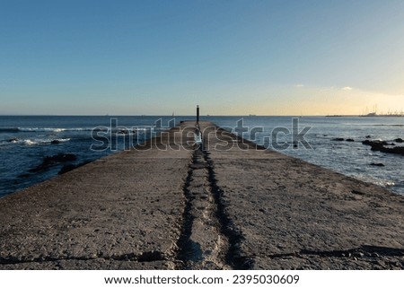 Concrete jetty with no people reaching away into the calm seas of the Atlantic Ocean at sunset in Cascais in Portugal