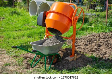 concrete is loaded into a cart from a 200 liter orange electric concrete mixer, photo taken on a sunny summer day outdoors