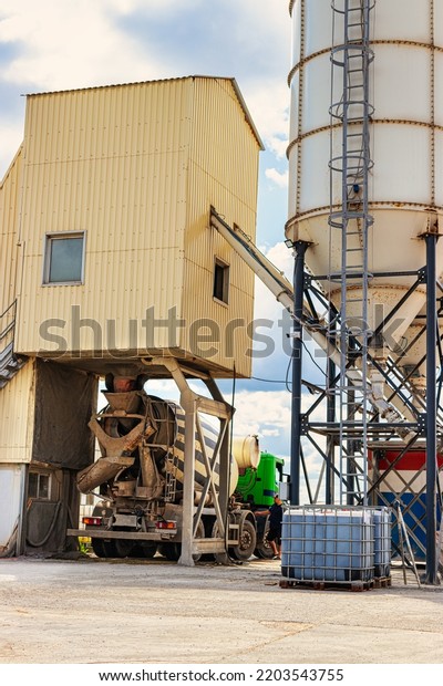 Concrete mixer truck in front of a\
concrete batching plant, cement factory. Loading concrete mixer\
truck. Close-up. Delivery of concrete to the construction site.\
