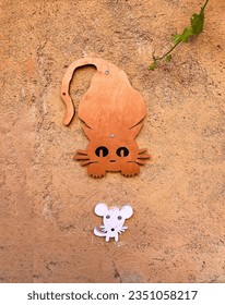 a concrete orange wall with orange wooden cat running after a white mouse, funny orange cat chasing a scaredy white mouse in a cement wall, vertical