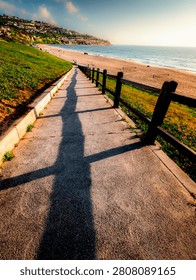 A concrete path leads down to a sandy beach and the ocean, with homes dotting the hillsides of Palos Verdes