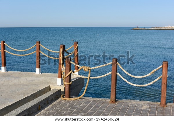 \
Concrete\
pier on the background of the seascape. A fence of wooden posts and\
a rope stretched between them. The concept of security. There is a\
long pier in the distance. Space for\
text.\
