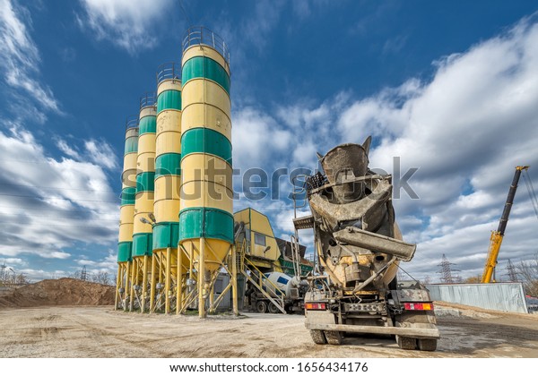 Concrete Plant. A\
concrete truck machine is awaiting loading near the cement storage\
towers. Sunny day, blue\
sky.
