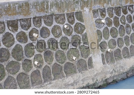 Concrete retaining wall structure with drainage pipes and stone pattern texture