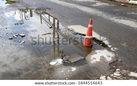The concrete road is damaged, potholes, and waterlogged due to rain, so a  traffic cone is used to alert drivers to drive carefully.