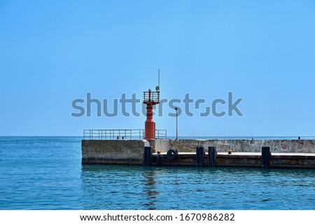 concrete sea berth or pier with signal beacon and with car tires for mooring boats and yachts and horizon of sea and sky