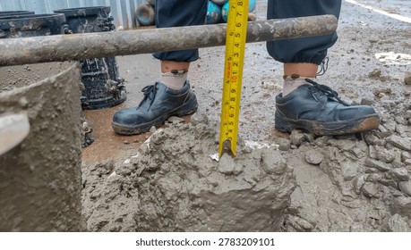 Concrete slump test in progress, measuring the workability and consistency of fresh concrete at a construction site with a yellow tape measure.