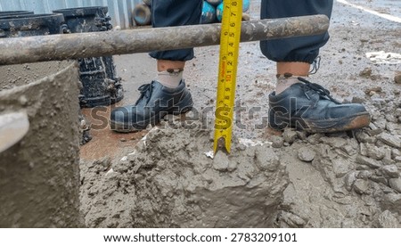 Concrete slump test in progress, measuring the workability and consistency of fresh concrete at a construction site with a yellow tape measure.