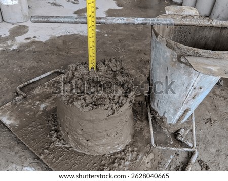 Concrete slump test in progress showing measurement of workability using slump cone and ruler on construction site.