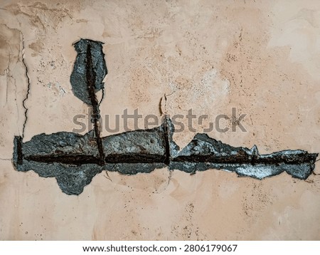 Concrete spalling exposing rusty rebar reinforcement on a weathered peach wall.