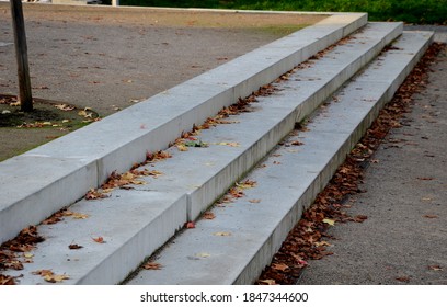 Concrete Stairs To The Park Serving At The Same Time As A Sitting Bench. Gray Cement Clean Smooth Bright Cement Surface. Granite Cubes Paving Threshing Gravel Road. Overgrown With Plants. Anti-slip