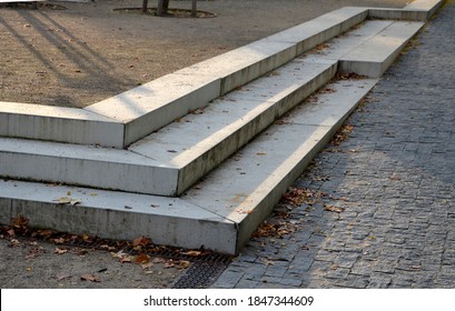 Concrete Stairs To The Park Serving At The Same Time As A Sitting Bench. Gray Cement Clean Smooth Bright Cement Surface. Granite Cubes Paving Threshing Gravel Road. Overgrown With Plants. Anti-slip