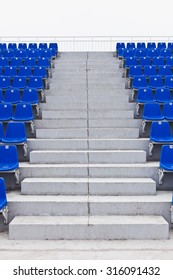 Concrete Steps Of Pathway Stairs On An University Stadium With Symmetrical Placed Blue Seats On Left And Right Sides Of Aisle. View From The Bottom Of Stairs To Top. Full Length Of Pathway. No People